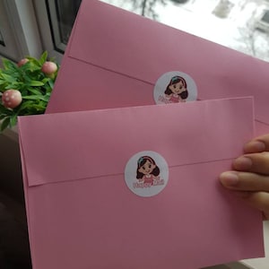 May include: Two pink envelopes with a cartoon girl sticker on each. The sticker on the top envelope says "Happy" and the sticker on the bottom envelope says "Happy Mail".