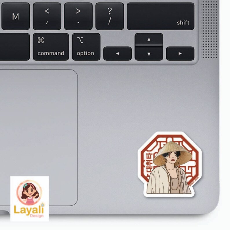 May include: A sticker featuring a cartoon illustration of a person wearing a conical hat and traditional clothing. The person is standing in front of a red octagon with the Korean text "대취타" written inside. The sticker is on a silver laptop.