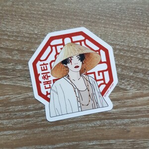 May include: A red octagon sticker with a white outline and a stylized image of a person wearing a conical hat and a white shirt. The sticker has Korean text that reads "대한민국".