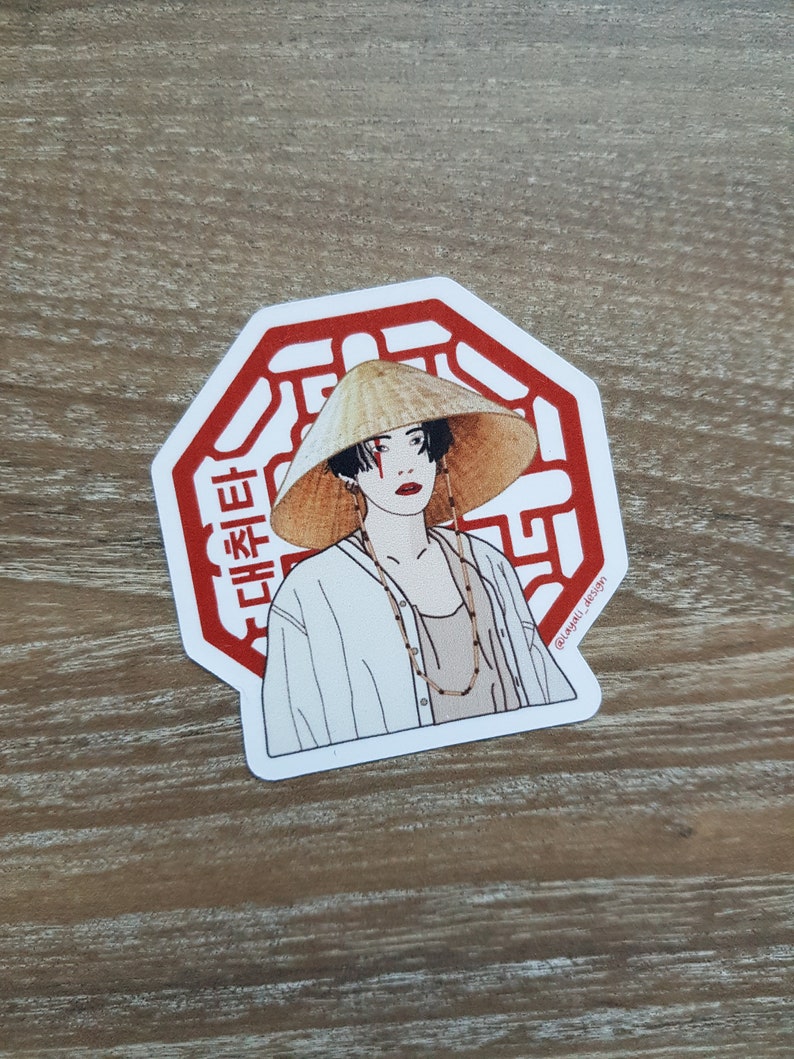 May include: A red octagon sticker with a white outline and a stylized image of a person wearing a conical hat and a white shirt. The sticker has Korean text that reads "대한민국".