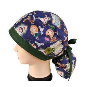 May include: A navy blue scrub cap with a green trim and a button closure. The cap features a repeating pattern of cartoon characters and Christmas-themed images. A green ribbon is tied at the back.