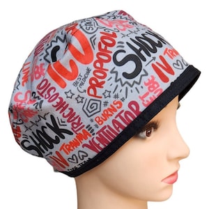 May include: Grey scrub hat with a black trim. The hat has a print of medical terms in red and black on a grey background. The text includes "Shock", "Propofol", "Trauma", "Burns", and "Ventilator".