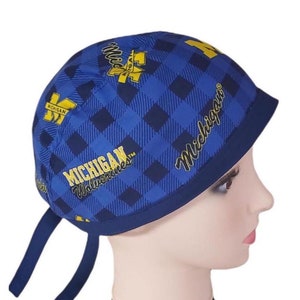 May include: Blue and yellow surgical scrub hat with a plaid pattern and the words "Michigan Wolverines" and "Michigan".