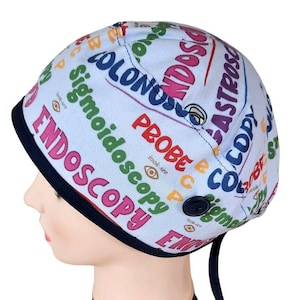 May include: A blue surgical scrub hat with a colorful print of medical terms, including "Endoscopy", "Probe", "Colonoscopy", and "Sigmoidoscopy". The hat has a button closure and a tie at the back.