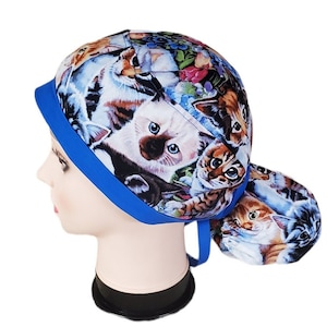 May include: A blue and cat-themed scrub cap. The cap features a vibrant pattern of various cat breeds, flowers, and foliage. The cap has a blue band and ties. The cap is designed to be worn in a medical or veterinary setting.
