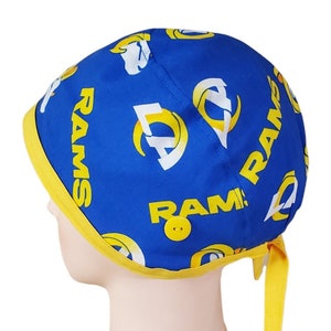 May include: Blue and yellow surgical scrub hat with a repeating pattern of the Los Angeles Rams logo and the word "RAMS".