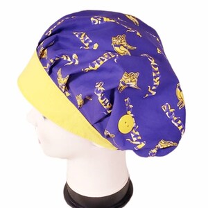 May include: A purple scrub cap with a yellow brim and a yellow button. The cap is patterned with yellow and white stylized animal figures. The cap is shown on a white mannequin head.