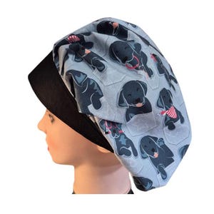 May include: A blue and black scrub hat with a pattern of black labrador retrievers. The hat has a black band around the bottom.