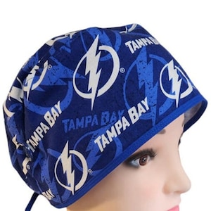 May include: Blue and white surgical scrub hat with a repeating pattern of lightning bolts and the words "Tampa Bay".