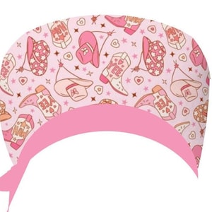 Op de afbeelding: Een roze operatiemuts met een herhalend patroon van cowboylaarzen, hoeden en sterren. De laarzen en hoeden hebben de woorden "Yee Haw" en "Love" erop. De muts heeft een effen roze band.