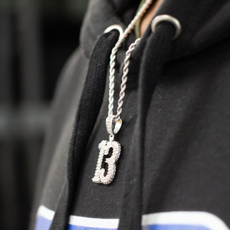 Puede incluir: Un collar de cadena de plata con un gran colgante en forma de n&uacute;mero "13" incrustado de diamantes.