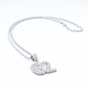 Puede incluir: Un collar de cadena de plata con un colgante que presenta el n&uacute;mero 82, incrustado con piedras de circonita c&uacute;bica transparentes.