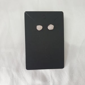 May include: A pair of rose quartz stud earrings on a black display card.
