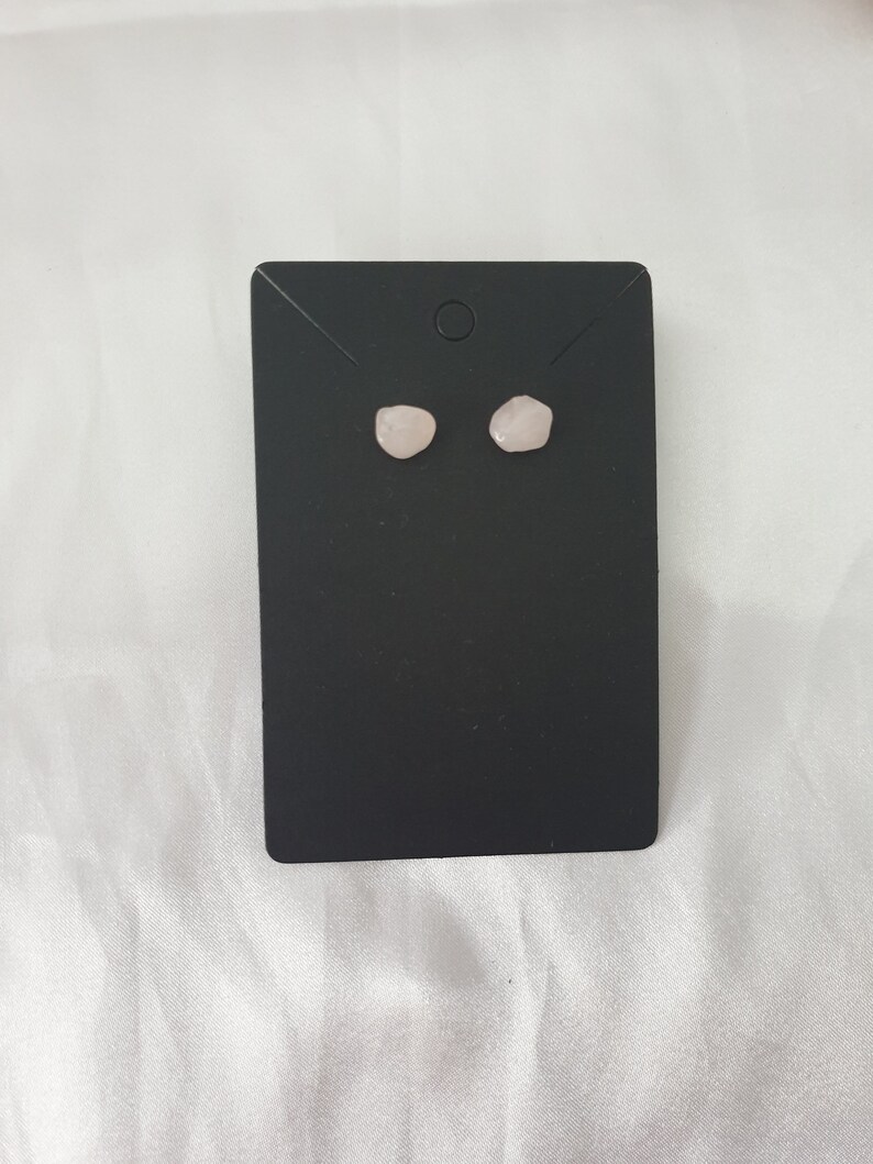 May include: A pair of rose quartz stud earrings on a black display card.