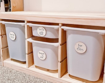 May include: A wooden storage unit with four white bins. The bins are labeled with wooden circles that say "Dress Up", "Train Set", "Dinosaurs", and "Lego".