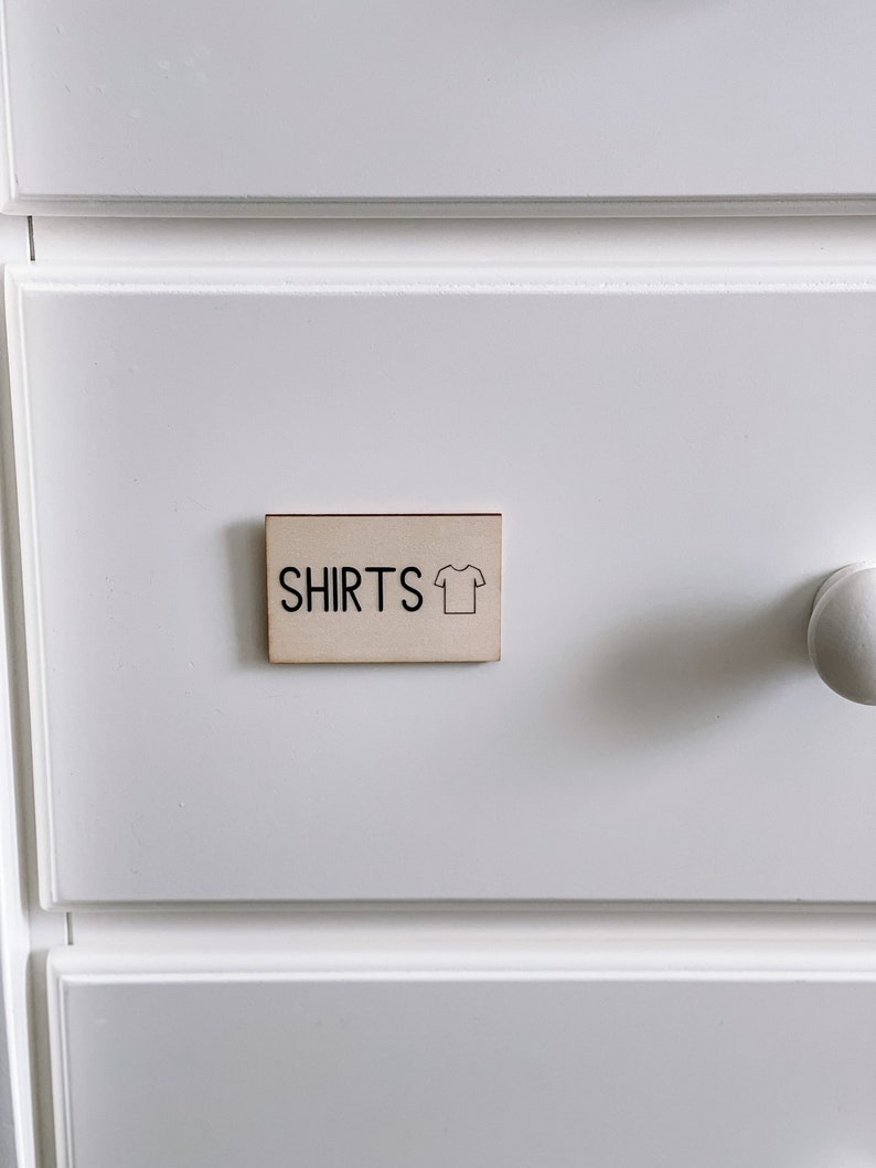 May include: A white drawer with a wooden label that says "SHIRTS" with a simple line drawing of a t-shirt.