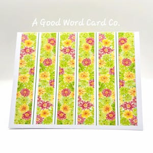 May include: A rectangular greeting card featuring the text A Good Word Card Co. at the top. The card displays five vertical panels of a floral pattern with watercolor-style flowers in shades of yellow, lime green, and magenta on a white background.