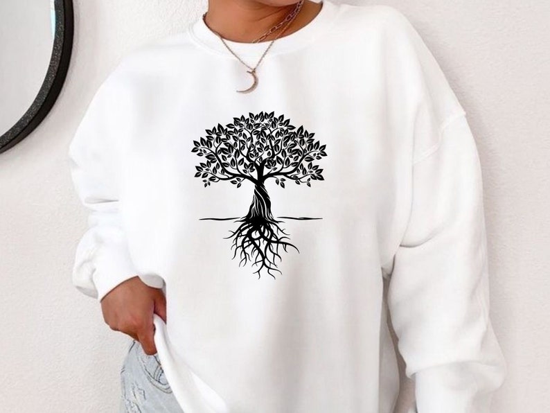 May include: White sweatshirt with a black tree design. The tree has a detailed trunk, leafy branches, and exposed roots. The design is centered on the front. The sweatshirt has long sleeves and a crew neck.