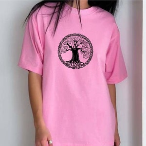 May include: A pale pink t-shirt with a black tree of life design inside a circular Celtic knot border. The short-sleeved shirt is made of a soft material.