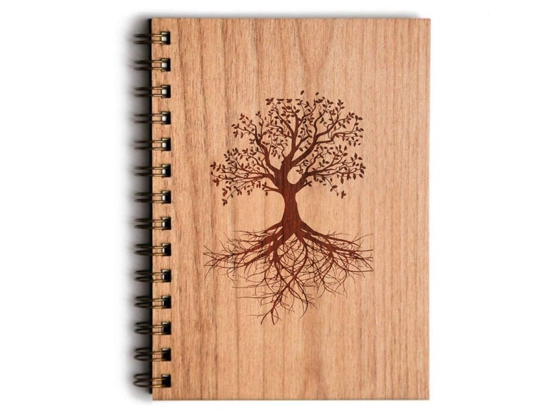 May include: A wooden notebook with a spiral binding, featuring a laser-etched tree design. The tree has a detailed trunk, branches, leaves, and roots. The cover is made of light-coloured wood, and the spiral binding is a dark metal.