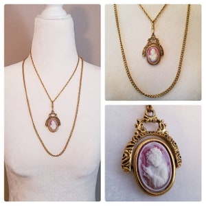 May include: A gold chain necklace with a cameo pendant featuring a woman's profile in pink and white. The pendant is attached to a swivel clasp.