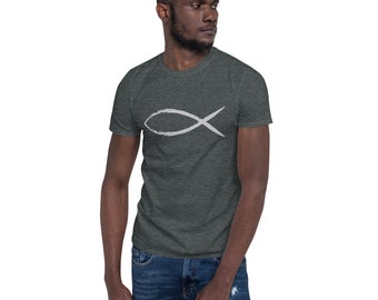 May include: Dark gray t-shirt featuring a white Ichthys symbol, a Christian symbol resembling a fish. The short-sleeved shirt is made of a soft material and is paired with blue jeans. The design is simple and minimalist.