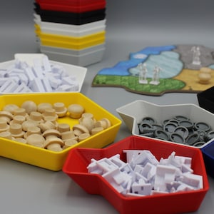 Könnte beinhalten: Ein Satz von sechs sechseckigen Spielsteinspeicherbehältern in Gelb, Rot, Weiß, Grau, Blau und Schwarz. Die Behälter sind mit verschiedenen Spielsteinen gefüllt, darunter kleine Holzstücke, Plastikteile und Metallteile.