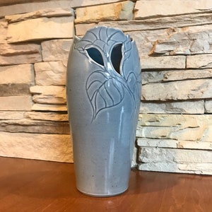 May include: A light blue ceramic vase with a floral design. The vase has two cut-out openings in the shape of leaves.