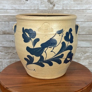 May include: A blue and white stoneware crock with a bird and floral design. The crock has two handles and a wide mouth.