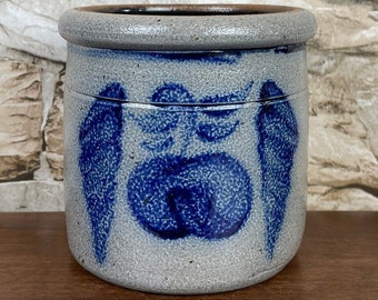 May include: A gray stoneware crock with a blue and white design of apples and leaves. The crock has a rough, textured surface.