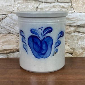 May include: A white ceramic crock with a blue apple design. The crock has a rounded shape and a wide opening.