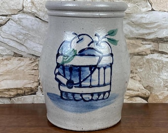 May include: A gray stoneware crock with a blue and white painted design of a basket of apples. The basket is painted with blue and white stripes and has a handle. The apples are painted in shades of white and green.