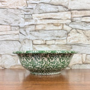 May include: A round bowl featuring a white base with a green speckled, splatter-style pattern across the entire exterior surface. The bowl has a smooth, rounded rim and a slightly tapered base, presenting a consistent mottled design throughout.