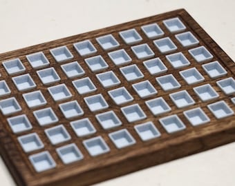 May include: A wooden watercolor paint palette with a grid of 56 small, square, light blue paint wells. The palette is made of dark brown wood with a raised edge. The paint wells are empty.