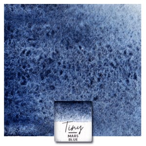 Op de afbeelding: Een vierkant aquarelverf napje met het label Tiny MARS BLUE, voorzien van een diep marineblauw pigment met een korrelige textuur. De verf verloopt van een donker, verzadigd blauw aan de bovenkant naar een lichtere, vervaagde blauwtint onderaan.