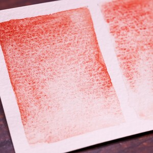 May include: Two watercolour swatches on white paper. The left swatch is a gradient of red to white. The right swatch is a gradient of red to white with a vertical brushstroke pattern.