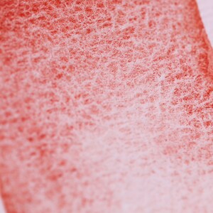 May include: Close-up of a red watercolour wash on paper. The wash is uneven and has a grainy texture. The paper is white and has a slight texture.