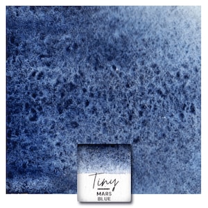 Könnte beinhalten: Eine Nahaufnahme einer Aquarellfarbprobe in einem kleinen quadratischen Behälter. Die Farbe ist tiefblau mit einem Farbverlauf von dunkel nach hell. Das Etikett auf dem Behälter lautet "Tiny Mars Blue".