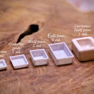 May include: Five watercolour paint pans of different sizes, from smallest to largest: mini pan (0.5 ml), quarter pan (1 ml), half pan (2 ml), full pan (4 ml), and ceramic half pan (2 ml).