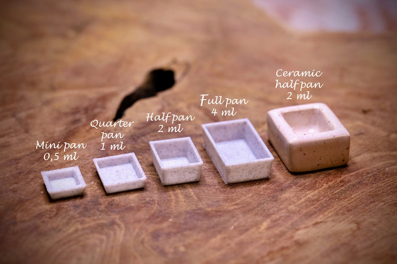 May include: Five watercolour paint pans of different sizes, from smallest to largest: mini pan (0.5 ml), quarter pan (1 ml), half pan (2 ml), full pan (4 ml), and ceramic half pan (2 ml).