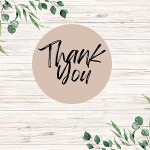 May include: A round, light brown sticker with the words "Thank You" in black script. The sticker is set against a light wood background, with green eucalyptus leaves and branches in the corners.