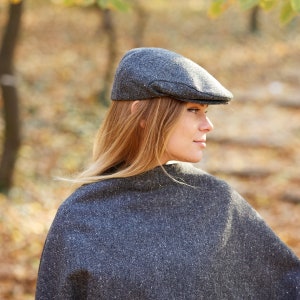 May include: A woman wearing a grey tweed newsboy cap and a matching grey tweed poncho. The cap has a slightly curved brim and a small button on top.