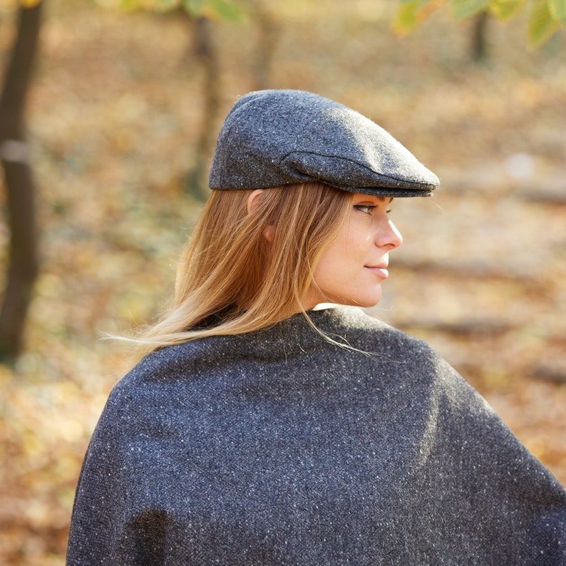 May include: A woman wearing a grey tweed newsboy cap and a matching grey tweed poncho. The cap has a slightly curved brim and a small button on top.