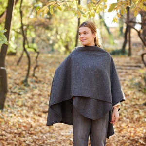May include: A woman wearing a grey wool poncho in a woodland setting. The poncho has a simple design and is made of a soft, warm fabric.