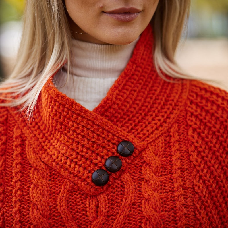 May include: A close-up of a bright orange knitted sweater with a cable knit pattern and three brown buttons on the collar.