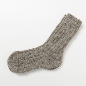 Könnte beinhalten: Eine einzelne graue Wollsocke mit geripptem Strickmuster. Die Socke besteht aus einem gesprenkelten Garn, und der Bund ist umgeschlagen. Die Socke ist für den linken Fuß bestimmt.