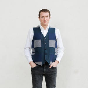 Puede incluir: Un chaleco patchwork en tonos azul marino, verde azulado y gris. El chaleco tiene cuello en V y cierre de botones. La persona lleva una camisa blanca y vaqueros negros. El chaleco es una elegante adición a cualquier guardarropa.