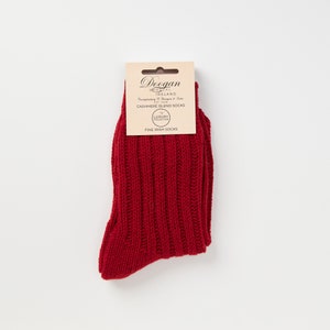 Op de afbeelding: Rode sokken van een cashmere-mix met een geribbelde textuur. De sokken zijn verpakt met een label waarop staat "Doogan Donegal Ireland Est. 1958  Incorporating Style, Design & Care  Cashmere Blend Socks Luxury Collection Fine Irish Socks".