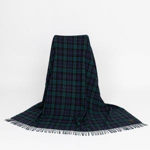 Peut inclure: Une couverture à carreaux bleu marine et vert avec une bordure à franges. La couverture est drapée sur une chaise, mettant en valeur son motif. Le motif à carreaux présente un quadrillage de lignes entrecroisées en vert foncé et bleu marine.