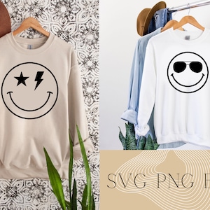 May include: Two white sweatshirts with black smiley face designs. One smiley face has a star and lightning bolt for eyes. The other smiley face has sunglasses. The text "SVG PNG EPS" is on a tan background with white wavy lines.